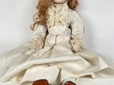 doll sitting on a white surface wearing a white dress and red shoes