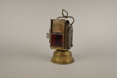 une vieille lanterne en laiton avec un verre rouge à l'intérieur, posée sur une surface blanche