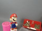 a small plastic mario figure next to a pink cup