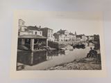 a black and white photo of a man sitting on the bank of a river