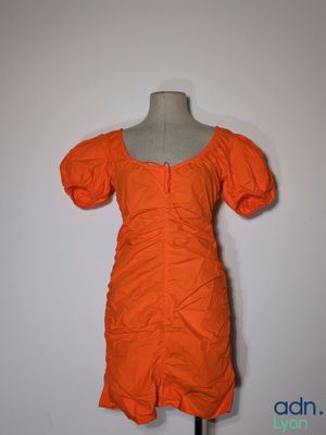 une robe orange posée sur un mannequin, devant un mur blanc