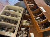 several trays of silverware sit on a table in a store