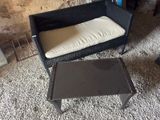 une chaise en osier noir avec un coussin blanc, à côté d'une table basse