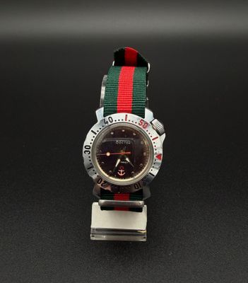 une montre avec un bracelet rouge et vert sur un cadran noir