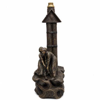 une statue représentant un homme assis sur un rocher, près d'un phare