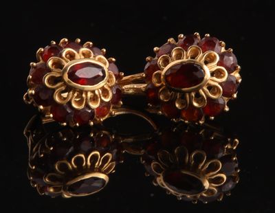 une paire de boucles d'oreilles en or ornées de grenats sur un fond noir