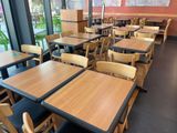 Dans un restaurant doté d'une grande baie vitrée, les tables et les chaises sont alignées.