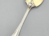 an antique silver spoon with a spoon handle on a gray surface