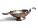 a silver bowl with a spoon in it on a white surface