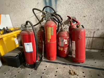 Plusieurs extincteurs sont alignés sur une étagère à côté d'une boîte jaune