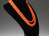 an orange beaded necklace on a black mannequin stand