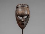 a close up of a wooden mask on a metal stand