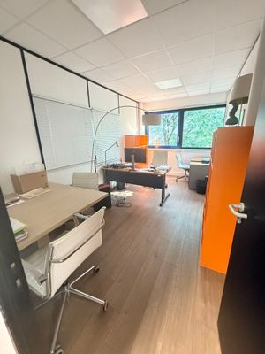 une pièce avec un bureau, des chaises, un fauteuil, une lampe et une grande fenêtre