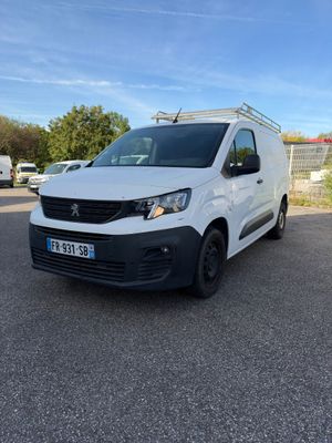 La camionnette blanche est garée sur le parking, à côté d'une clôture.
