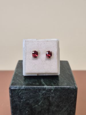 une paire de boucles d'oreilles à clous ornées de grenats rouges, posée sur un bloc de marbre