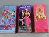 two barbie and ken dolls are sitting side by side on a table