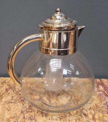 un pichet en verre avec un couvercle en argent posé sur une table