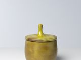 petit pot en céramique jaune avec couvercle, posé sur une surface blanche