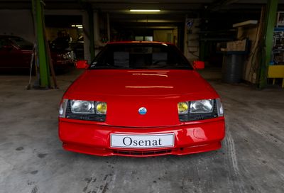 une voiture rouge garée dans un garage, avec une plaque d'immatriculation