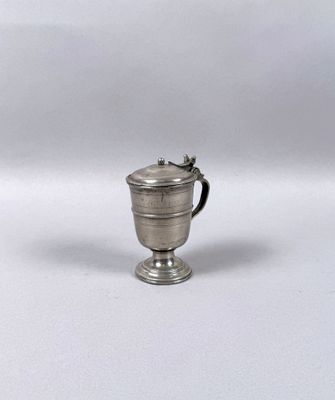 an antique silver cup with a handle on a white surface