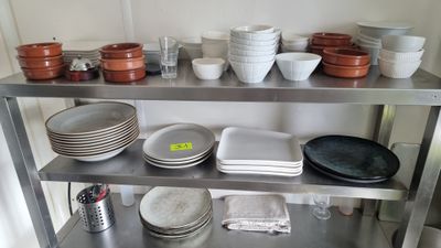 Plusieurs assiettes et bols sont empilés sur une étagère en métal dans une cuisine