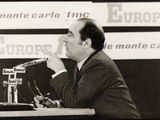 photographie en noir et blanc d'un homme en costume parlant dans un micro