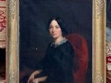 portrait d'une femme en robe noire, assise sur une chaise rouge
