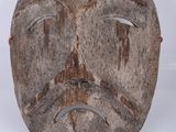un vieux masque en bois posé sur une surface blanche, avec un fond blanc