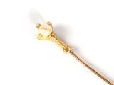 a gold stick with a pearl on it on a white surface