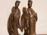 une paire de figurines asiatiques posées sur une table en bois, avec un mur blanc en arrière-plan