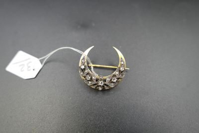 une broche en forme de croissant, en or et diamants, posée sur un fond noir