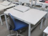 de nombreux bureaux et chaises dans un entrepôt, avec un ordinateur posé dessus