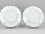 two white plates with gold rims on stands on a gray surface