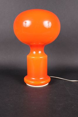 une lampe de table orange avec un cordon blanc posée sur une surface noire