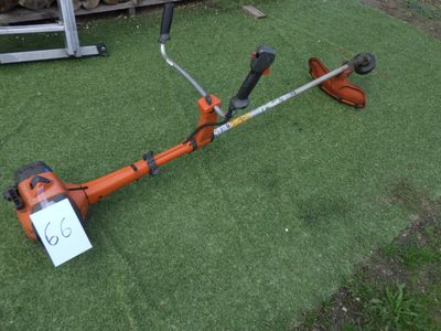 une débroussailleuse orange posée au milieu d'un champ recouvert d'herbe