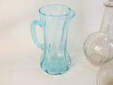 un pichet en verre bleu à côté d'une bouteille en verre transparent
