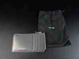 un portefeuille et une pochette en cuir noir posés sur une table noire, à côté d'un sac noir