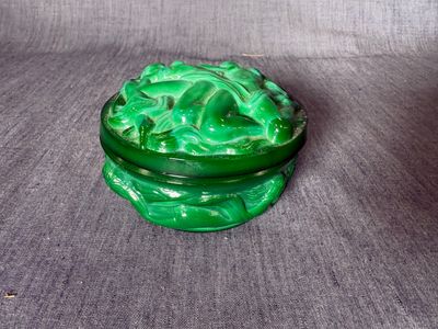 une image représentant une boîte en verre vert posée sur une surface grise