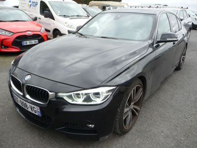 une BMW Série 3 noire garée sur un parking, avec d'autres voitures en arrière-plan