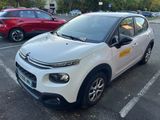La petite voiture blanche est garée sur le parking, à côté d'autres voitures.