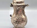 une cafetière ancienne en métal argenté, avec couvercle, posée sur un socle