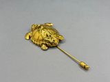 une image représentant une broche en forme de tortue dorée posée sur une surface grise