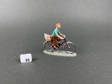 a figurine of a man riding a bike with a dog in a basket