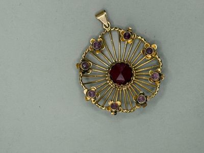 a close up of a gold pendant with a red stone