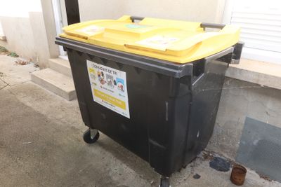 a black trash can with a yellow lid sitting on a sidewalk