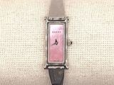 une montre rose avec un bracelet en cuir noir, posée sur un coussin blanc