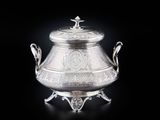 une théière ancienne en métal argenté sur socle, ornée de motifs élaborés