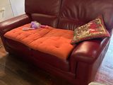 a red leather couch with a pillow on it in a living room
