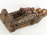 wooden statue of a man laying on a bed with his head resting on a pillow