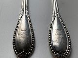 pair of silver spoons with designs on them sitting on top of a table